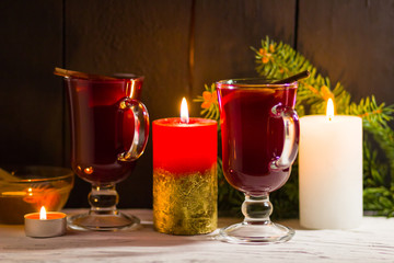 Mulled wine and burning candle on dark background. Christmas mulled wine, cinnamon sticks and honey. Alcohol drink of wine and honey. Festive drink and Christmas tree branches