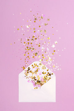 Golden and pink confetti pouring out of white envelope on pastel purple background. View from above. Flat lay. Holiday, congratulations or good news concept.
