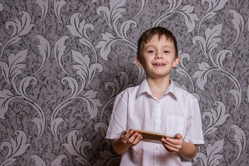 A boy in a white shirt is standing with a phone in his hands