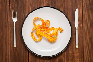 Empty plate with measure tape, knife and fork on the wooden background. Diet food concept top view