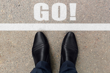 Feet on the street with text GO! Word GO! written on an asphalt road. Top view of the legs and shoes