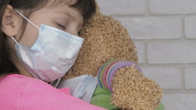 Ill girl with medical mask huggs her bear. Little girl in a protective mask with a teddy bear.
