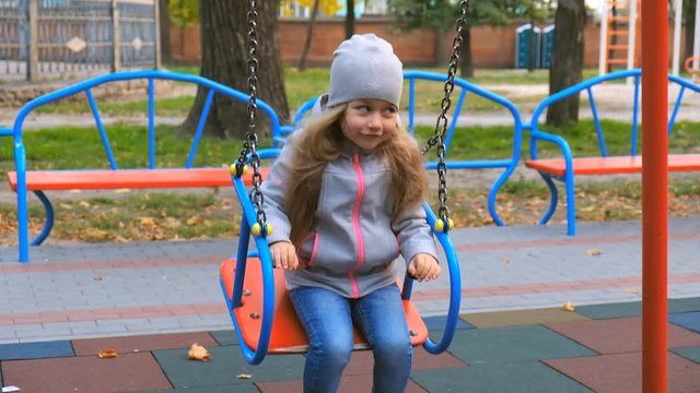 Little girl riding on a swing on the playground in the park in the fall.