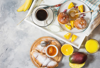 Breakfast served with coffee, orange juice, croissants, donuts and fruits on white tray.