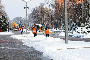 Workers in orange vests and a tractor clean the city street from fresh snow in the winter . Dnipro city, Dnepropetrovsk, Dnipropetrovsk,  Ukraine