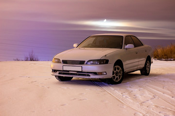 Fototapeta na wymiar white sports car in the snow at night with a full moon in the clouds