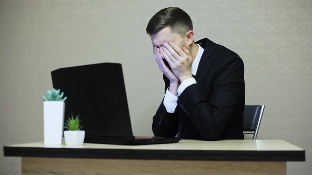 Businessman in suit crying in the workplace. He's upset, bad luck, then calms down