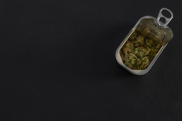 Tin can with high quality marijuana buds isolated on black background with copy space left. Packaged marijuana. Open aluminum box with weed inside.