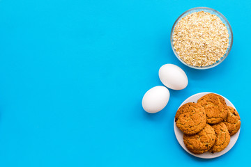 Ingredients for homemade cookies. Fresh cookies near oatmeal, eggs on blue background top view space for text