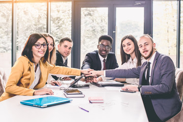Large business team showing unity with their hands together. Full concentration at work. Group of young business people working and communicating while sitting at the office desk