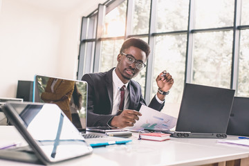 Businessman with laptop. Cheerful young African businessman typing something on laptop