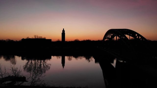 Sunrise at winter with bridge and tower silhouette at a river.