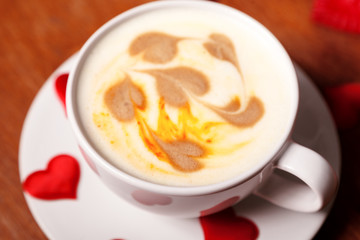 Valentine's day background. A white Cup of cappuccino coffee with a latte art in the form of hearts. Coffee on a wooden table covered with red hearts. Meeting with your loved one over a Cup of coffee