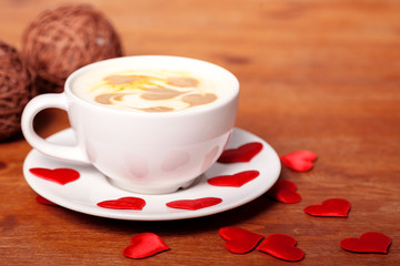 Valentine's day background. A white Cup of cappuccino coffee with a latte art in the form of hearts. Coffee on a wooden table covered with red hearts. Meeting with your loved one over a Cup of coffee