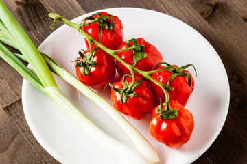 Red fresh cherry tomatoes on a white plate isolated on a wooden cutting board