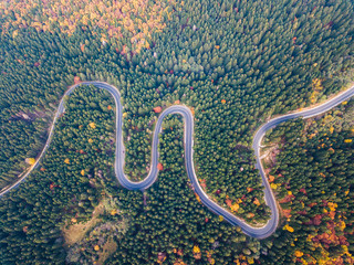 Winding road from mountain pass, in autumn season, with green and orange forest. Aerial view by drone. Romania	
