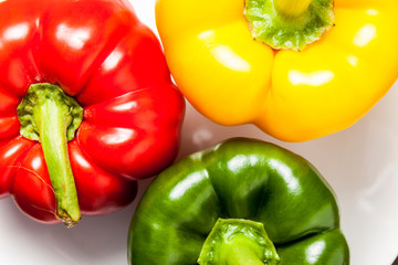 Red, yellow and green bell peppers on a white ceramic plate