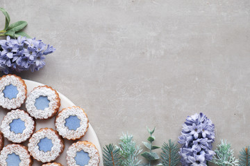Flower Linzer cookies with blue glazing on light concrete decorated with blue hyacinth flowers, fir twigs and herbs