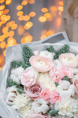 Winter bright bouquet of mixed flowers with cotton, pine branches Nobilis and Ranunculus. Floral Bunch with Persian buttercup in woman hands. Garland bokeh on background. Christmas love
