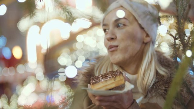 Happy attractive woman eating waffle with chocolate in a christmas market at night. Beautiful bokeh lights background.