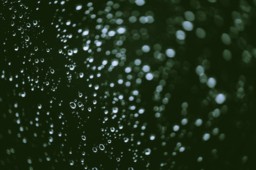 Dirty window glass with drops of rain. Atmospheric green background with raindrops in bokeh. Droplets and stains close up. Detailed transparent texture in macro with copy space. Rainy weather.