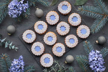 Top view of flower Linzer cookies with blue glazing on dark winter background with herbs and flowers