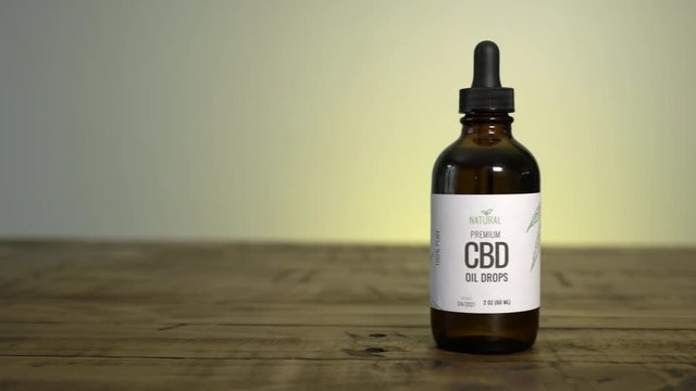 Camera panning to show dropper bottle of CBD oil on table.