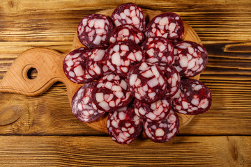 Sliced salami sausage on cutting board on wooden table. Top view