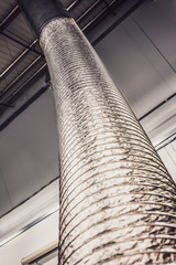 expandable metallic air-conditioning ventilation pipe or tube rising up to the ceiling inside a grey industrial type unit or factory
