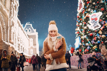Young woman with a cup of coffee walking on the winter street