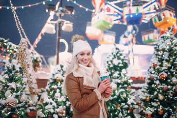 Young smiling female with a coffee cup on the winter new year street