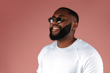 Obraz premium Man portrait. Style. Handsome Afro American guy in white T-shirt and sun glasses is smiling, on a pink background