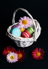 Sweet and colourful french macaroons in the basket on black background.