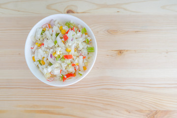 Salad with corn and crab sticks in white dish on wooden background top view with space for text