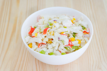 Salad with corn and crab sticks in white dish on wooden background. Selective focus
