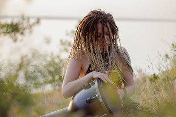 beautiful young woman hippie shaman playing djembe and dancing wild dances at sunset