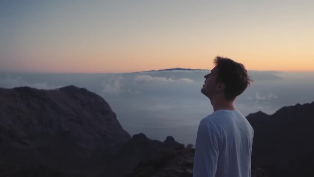 the man thoughtfully looks in the sky on the edge of the earth on top of the mountains above the clouds