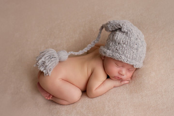 the first photo shoot. newborn child. the kid in the gray hat. the child lies on a beige blanket