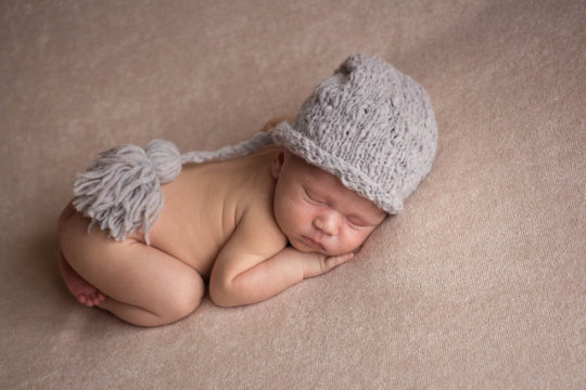 the first photo shoot. newborn child. the kid in the gray hat. the child lies on a beige blanket
