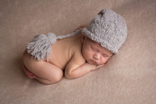 the first photo shoot. newborn child. the kid in the gray hat. the child lies on a beige blanket