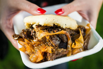 Close up photo of an arepa with lamb meat and caramelized onion at a street food market