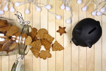 Oszczędności - świąteczny motw - świnka skarbonka, lampki i pierniki  w słoiku na drewnianym tle