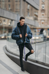 Fashionable man walk on the street near buildings. Wear blue jacket and all black. Winter, autumn outfit. Jacket with blouse and black sneakers.