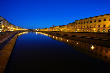 Fototapeta na wymiar Night view of colorful medieval buildings on the quay reflecting on the Arno River in Pisa, Tuscany, Italy