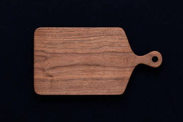 Handmade black walnut wooden chopping board on black cotton, walnut texture background.