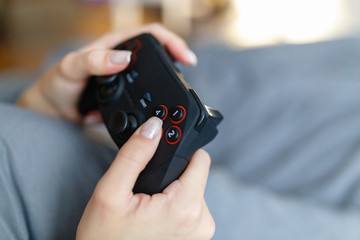Girl gamer playing video game with wireless joystick at home. Gamepad in female hands close-up, gaming addiction concept, woman gamer in underwear relaxes in the bed