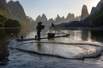 Silhouette of Chinese cormorant fisherman throwing a fishing net on a lake in Guilin China.