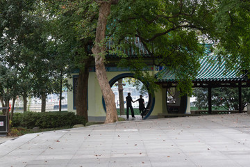 Dancing couple in silhouette outside during the day under a circular doorway in a Chinese building in East Lake park, Wuhan, China.