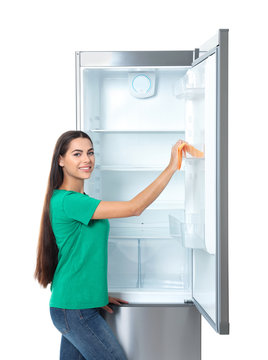 Young woman cleaning refrigerator with rag on white background