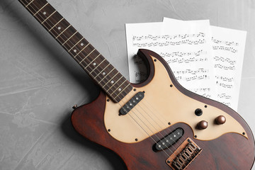 Modern electric guitar and music sheets on color background, top view